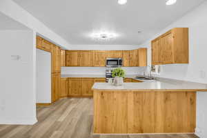 Kitchen with appliances with stainless steel finishes, sink, light wood-type flooring, and kitchen peninsula