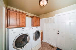 Laundry room featuring independent washer and dryer, cabinets, and light tile floors