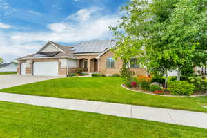 View of front of home with a front yard, a garage, and solar panels