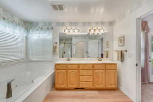 Bathroom with dual sinks, vanity with extensive cabinet space, a bathing tub, and hardwood / wood-style flooring