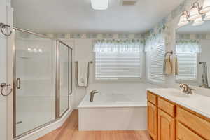 Bathroom with a wealth of natural light, wood-type flooring, vanity with extensive cabinet space, and shower with separate bathtub