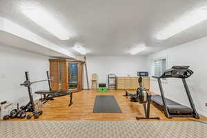 Exercise area with a textured ceiling and light wood-type flooring