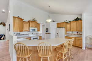 Kitchen with light hardwood / wood-style floors, white appliances, decorative light fixtures, a breakfast bar, and high vaulted ceiling