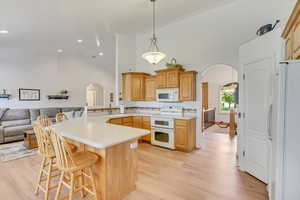 Kitchen with light hardwood / wood-style flooring, kitchen peninsula, a breakfast bar area, high vaulted ceiling, and white appliances