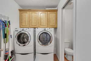 Laundry room featuring a textured ceiling, washer and clothes dryer, hardwood / wood-style flooring, and cabinets