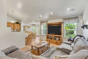 Living room featuring a wealth of natural light, vaulted ceiling, a notable chandelier, and light hardwood / wood-style flooring