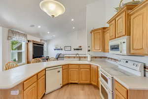 Kitchen featuring light wood-type flooring, white appliances, kitchen peninsula, sink, and vaulted ceiling