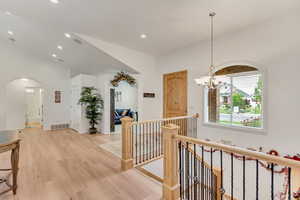 Hallway featuring vaulted ceiling, a chandelier, and light hardwood / wood-style floors