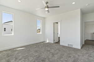 Unfurnished bedroom with carpet, multiple windows, ensuite bath, and ceiling fan