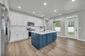 Kitchen with a center island with sink, appliances with stainless steel finishes, tasteful backsplash, and light wood-type flooring