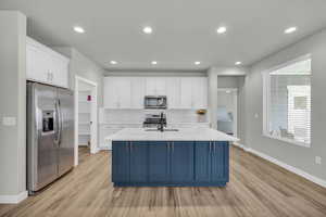 Kitchen featuring light hardwood / wood-style floors, appliances with stainless steel finishes, an island with sink, white cabinets, and backsplash