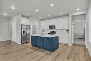 Kitchen with appliances with stainless steel finishes, a kitchen island with sink, light hardwood / wood-style floors, and tasteful backsplash