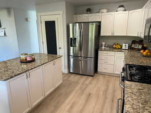 Kitchen featuring waterproof vinyl floor, Granite Countertops, Single Basin Sink with Sprayer, a kitchen island, a breakfast bar, and stainless steel appliances