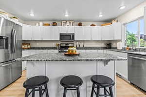 Kitchen featuring waterproof vinyl floor, Granite Countertops, Single Basin Sink with Sprayer, a kitchen island, a breakfast bar, and stainless steel appliances