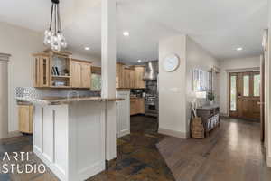 Kitchen featuring dark hardwood / wood-style floors, tasteful backsplash, light brown cabinetry, hanging light fixtures, and wall chimney exhaust hood