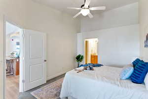 Carpeted bedroom with high vaulted ceiling, connected bathroom, and ceiling fan