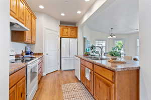 Kitchen featuring an inviting chandelier, light hardwood / wood-style floors, an island with sink, sink, and white appliances