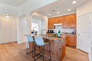 Kitchen with light stone countertops, light hardwood / wood-style flooring, a kitchen island with sink, a breakfast bar area, and sink