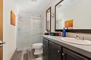 Bathroom with a shower with shower door, hardwood / wood-style floors, toilet, and vanity with extensive cabinet space