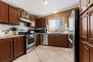 Kitchen with tasteful backsplash, light stone countertops, appliances with stainless steel finishes, sink, and light tile floors