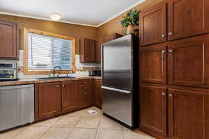 Kitchen with backsplash, sink, light tile flooring, and appliances with stainless steel finishes