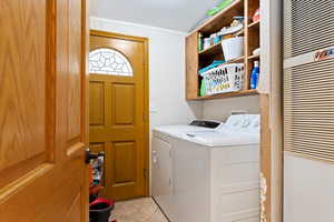 Laundry room with light tile floors, crown molding, and washing machine and dryer