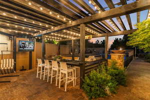 Patio terrace at dusk featuring a pergola and an outdoor bar