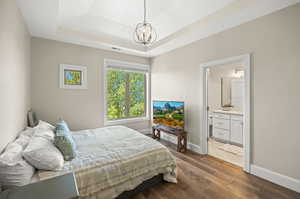 Bedroom with a chandelier, dark wood-type flooring, connected bathroom, and a raised ceiling