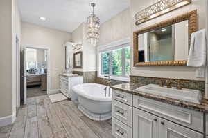 Bathroom with a bath to relax in, an inviting chandelier, vanity, and backsplash