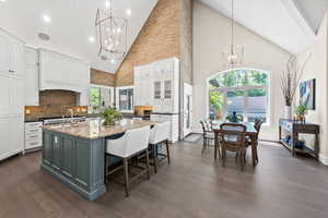 Kitchen with white cabinetry, dark hardwood / wood-style flooring, a kitchen island with sink, high vaulted ceiling, and a kitchen bar