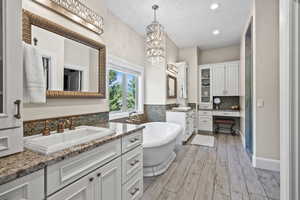 Bathroom featuring a bath to relax in, hardwood / wood-style flooring, backsplash, large vanity, and dual sinks