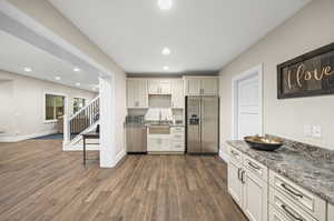 Kitchen with appliances with stainless steel finishes, sink, light stone countertops, and dark hardwood / wood-style flooring