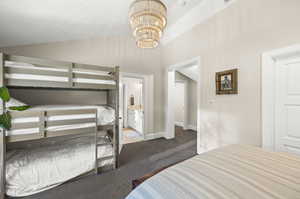 Carpeted bedroom featuring a chandelier, ensuite bathroom, and vaulted ceiling