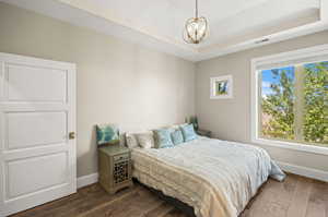 Bedroom with a tray ceiling, dark hardwood / wood-style floors, and a notable chandelier