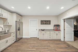 Kitchen with light stone countertops, sink, high end fridge, and wood-type flooring