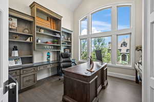 Office space with built in desk, lofted ceiling, and dark wood-type flooring