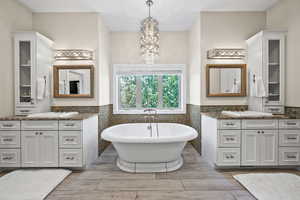 Bathroom with tile walls, an inviting chandelier, a washtub, and dual bowl vanity