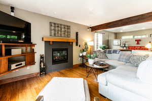 Living room featuring beam ceiling, a tiled fireplace, and hardwood / wood-style floors