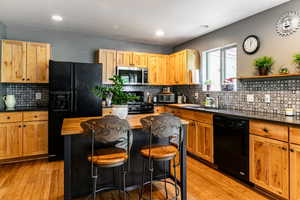 Kitchen with butcher block counters, backsplash, black appliances, and light hardwood / wood-style flooring