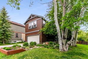 View of front of home featuring a garage and a front yard with flower beds and mature trees.