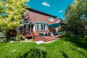 Rear view of property featuring a pergola, a wooden deck, and a lawn