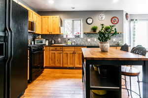 Kitchen with tasteful backsplash, light wood-type flooring, black appliances, wood counters, and a kitchen bar