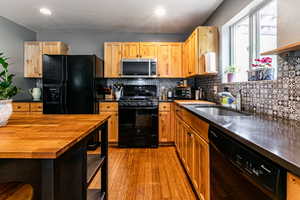 Kitchen featuring light hardwood / wood-style flooring, tasteful backsplash, butcher block counters, black appliances, and sink