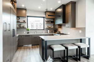 Kitchen with light hardwood / wood-style flooring, backsplash, hanging light fixtures, a kitchen bar, and sink