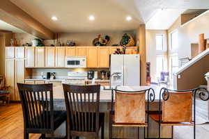 Kitchen featuring white appliances, a breakfast bar area, light wood-type flooring, and light brown cabinets