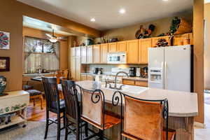 Kitchen with white appliances, a kitchen island with sink, light wood-type flooring, and ceiling fan