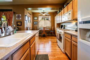 Kitchen with ceiling fan, light hardwood / wood-style flooring, white appliances, and sink