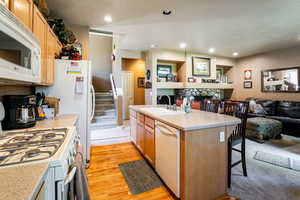 Kitchen featuring light hardwood / wood-style floors, a kitchen breakfast bar, white appliances, a kitchen island with sink, and sink