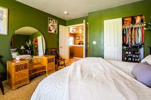 Bedroom with ensuite bathroom, a closet, a textured ceiling, and carpet floors