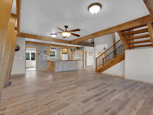 Unfurnished living room with beamed ceiling, ceiling fan, and light wood-type flooring